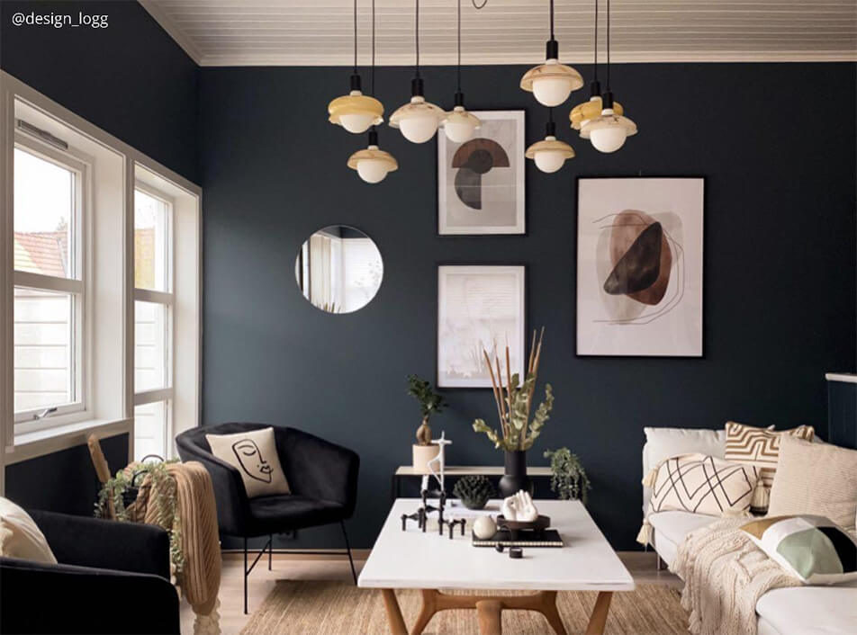 Vardagsrum med mörka väggar, svarta sammetsfåtöljer, rund spegel, grafiska posters